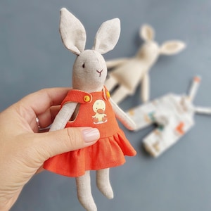 May include: A handmade plush bunny toy wearing a red dress with a yellow duck applique. The bunny has long ears and a sweet face.