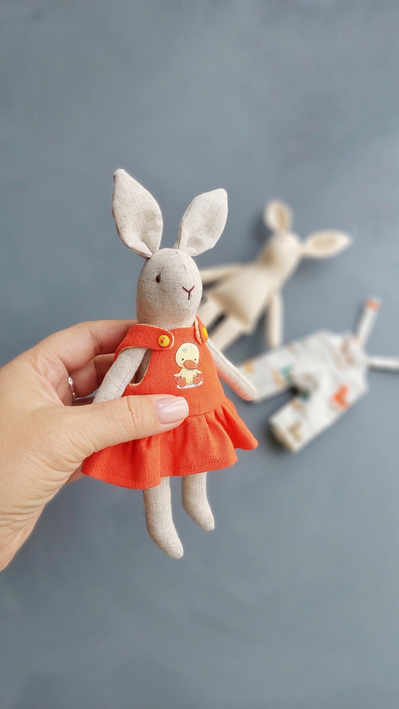 May include: A handmade plush bunny toy wearing a red dress with a yellow duck applique. The bunny has long ears and a sweet face.