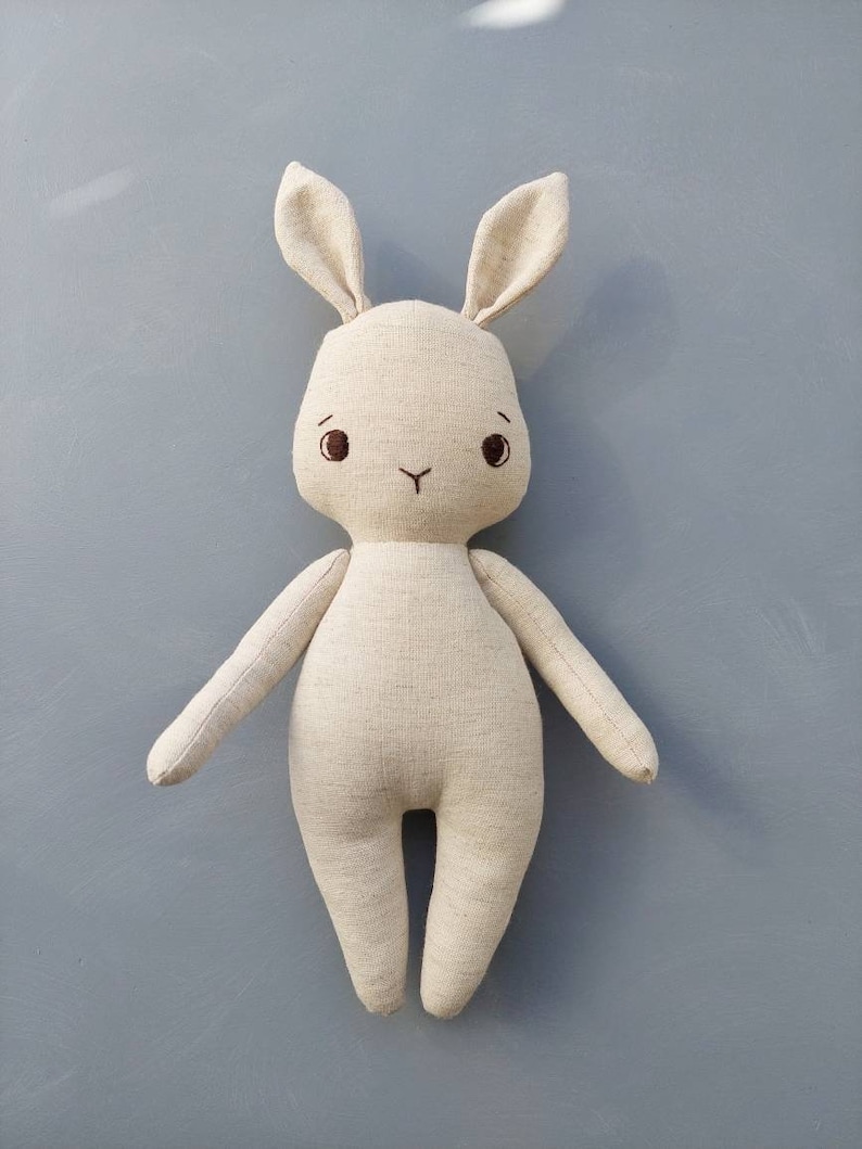 May include: A beige linen bunny rabbit stuffed animal with embroidered eyes and a nose.