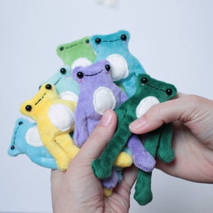 May include: A collection of plush frog toys in various colors, including yellow, green, blue, and purple. The frogs have white bellies and black eyes.
