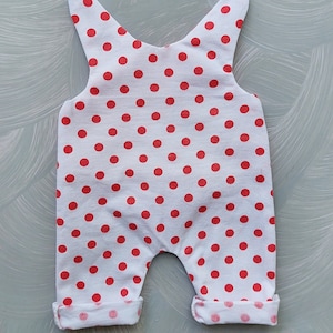 May include: White baby onesie with red polka dots. The onesie has a sleeveless design and cuffed legs.