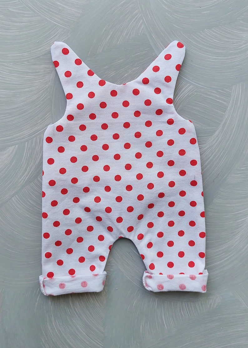 May include: White baby onesie with red polka dots. The onesie has a sleeveless design and cuffed legs.
