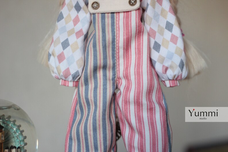 May include: A pair of striped overalls with a blue and white stripe on one leg and a pink and white stripe on the other leg. The overalls have a white bib with two buttons and are made of a soft, cotton fabric.