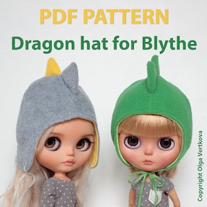 May include: PDF pattern for a dragon hat for Blythe dolls. The hat is shown in two colors, grey and green, with yellow accents. The hat has a pointed ear and a long tail.