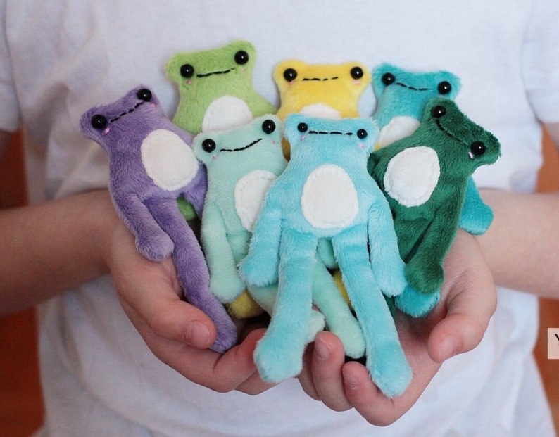 May include: A collection of eight plush frog toys in various colors, including purple, green, blue, yellow, and light green. The frogs have white bellies and black eyes.
