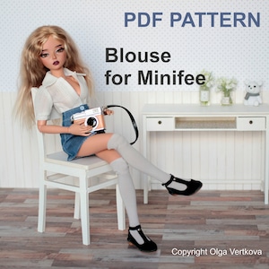 Peut inclure: Patron PDF pour un chemisier pour une poupée Minifee. Le patron est présenté sur une poupée portant un chemisier blanc, une jupe en jean et des chaussettes blanches montantes. La poupée est assise sur une chaise blanche et tient un appareil photo.