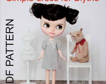 Puede incluir: Un patrón PDF para un vestido sencillo para una muñeca Blythe. La muñeca lleva el vestido y tiene el pelo castaño y los ojos verdes. La muñeca está sentada en una silla blanca con un oso de peluche.