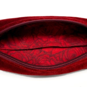 Può includere: Un astuccio per matite in velluto rosso con una fodera floreale rossa. L'astuccio è aperto e la cerniera è tirata verso il basso.