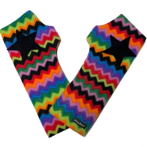 May include: A pair of colorful fingerless gloves with a vibrant chevron pattern in rainbow hues. Each glove features a large black star appliqué. The gloves are made of a soft material and are designed to keep hands warm.