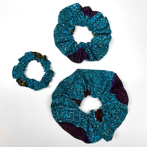 Puede incluir: Tres scrunchies de tela azul turquesa con un diseño estampado marrón y amarillo. Los scrunchies son de diferentes tamaños.