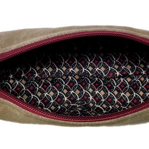 Puede incluir: Una bolsa de cremallera beige con una cremallera roja y un forro estampado en blanco y negro.