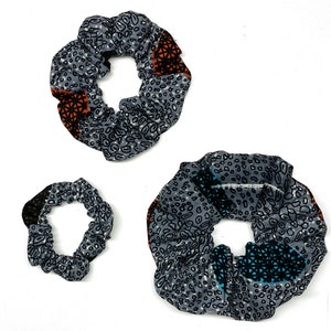 Puede incluir: Tres coleteros grises con un patrón repetido de pequeñas formas blancas y negras. Cada coletero tiene un color de acento diferente, incluyendo naranja, negro y turquesa. Los coleteros están hechos de tela y están diseñados para sujetar el cabello.