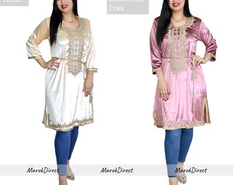 May include: Two women are wearing long-sleeved, knee-length dresses with gold embroidery. The dress on the left is ivory and the dress on the right is pink. Both women are wearing blue jeans and heels.