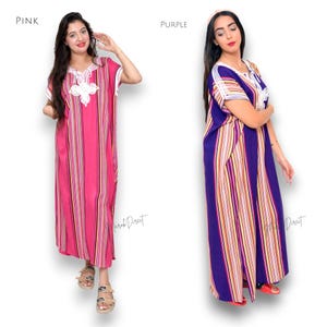 May include: Two floor-length kaftan dresses, one in pink and one in purple, both featuring vertical multi-colored stripes, short sleeves, and a white embroidered V-neckline detail. The text "PINK" and "PURPLE" labels the respective garments.
