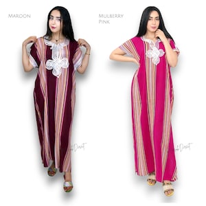 May include: Two floor-length kaftan dresses featuring vertical stripes in shades of maroon or mulberry pink, accented with white, orange, and purple lines. Each dress has short sleeves, a round neckline, and white embroidered detailing on the chest.