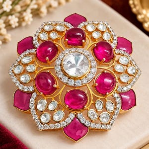 May include: A gold-toned brooch featuring a large central clear stone surrounded by a halo of small white crystals. The design includes six oval-shaped deep pink cabochon stones and six petal-shaped pink stones, all accented with white crystals.