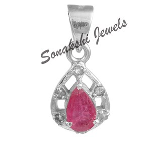 May include: A silver pendant with a teardrop-shaped, deep red gemstone at its center. The pendant is surrounded by a decorative openwork design and small, clear accent stones. The text "Sonakshi Jewels" is printed on the image.