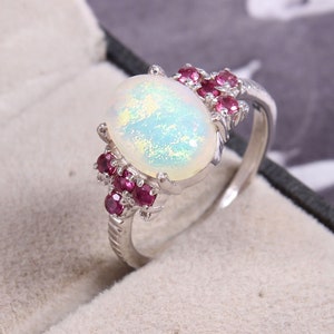 May include: A silver ring with a large white opal gemstone and smaller pink gemstones around the setting.