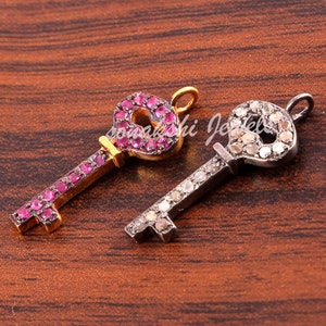 May include: Two gold key charms, one with pink gemstones and one with clear gemstones. Both charms have a detailed key design.