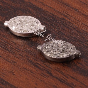 Peut inclure: Deux breloques ovales en argent avec un sertissage pavé de petits diamants blancs. Les breloques ont une finition lisse et polie et sont parfaites pour ajouter une touche d'éclat à tout projet de bijoux.
