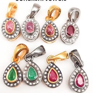 May include: A collection of gemstone pendants in various shapes and colors. The pendants feature oval and teardrop designs with gold and silver-toned bails. Gemstones include pink, red, and green stones, each surrounded by a halo of small, clear stones. The brand name "Sonakshi Jewels" is visible.