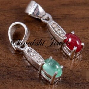 May include: Two silver pendants featuring oval-cut gemstones. One pendant holds a deep red stone, while the other contains a light green stone. Each piece includes a bail and a vertical bar set with small clear stones leading to the main gem.