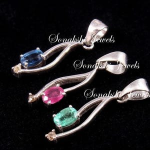 May include: Three silver-toned pendants, each featuring a curved metal frame, a small clear accent stone at the tip, and a central oval-cut gemstone in blue, pink, or green. Each pendant includes a bail and the text Sonakshi Jewels.