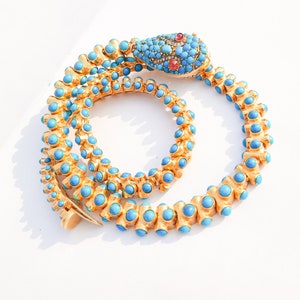 May include: A gold snake necklace with turquoise and ruby stones. The snake's head is detailed with a ruby eye and a diamond-encrusted crown.