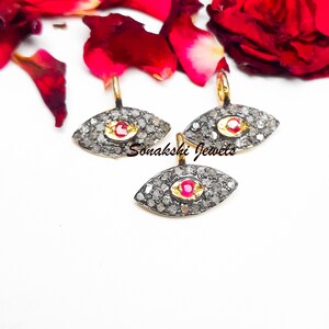 May include: Three gold evil eye charms with a red ruby center and pave set diamonds. The charms are on a white background.
