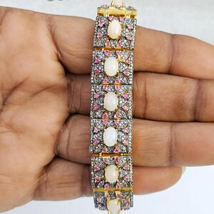 Puede incluir: Un brazalete de oro con una fila de ópalos ovalados engastados en un marco de plata y oro. El marco está decorado con pequeñas piedras rosas y blancas.