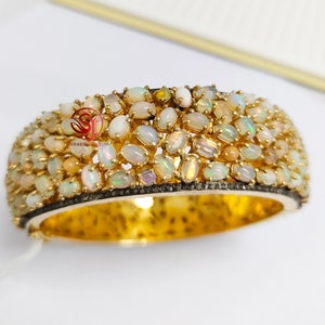 May include: A gold bangle bracelet with a row of white opal stones set in a gold frame. The bracelet is accented with a row of black diamonds.