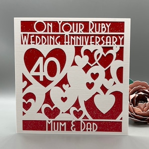 May include: A red and white card with a white heart design and the text "On Your Ruby Wedding Anniversary 40 Mum & Dad".