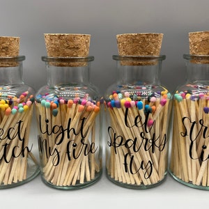 May include: Four glass jars filled with matches, each with a different saying on the front. The sayings are "Perfect Match", "Light My Fire", "Let Sparks Fly", and "Strike a Light".
