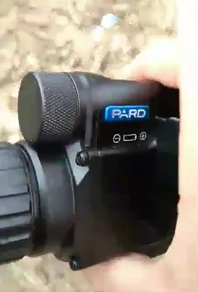 May include: A black night vision scope with a blue "PARD" logo and a black knob on the top. The scope has a black lens and a black body.