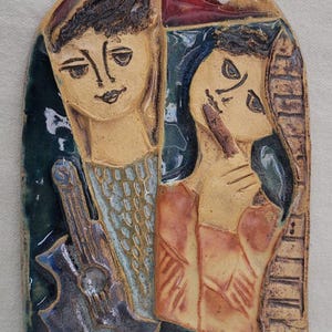 May include: A ceramic wall art piece featuring two stylized figures. One figure holds a guitar, the other touches their face. The artwork uses a palette of blues, browns, and reds, with a textured, glazed finish. The piece has an arched top.