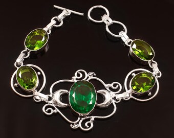 May include: A silver bracelet featuring oval-cut green gemstones. The bracelet has a decorative design with a central large stone and smaller stones linked by ornate silver settings. The clasp is a simple toggle.