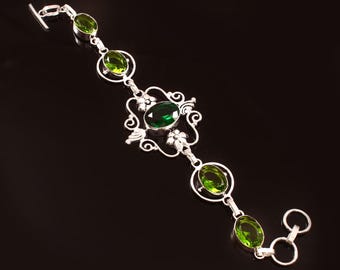 May include: A silver bracelet with oval-cut green gemstones. The bracelet features a central ornate design with a larger green stone, and smaller stones connected by silver links. The clasp is a simple hook and loop.