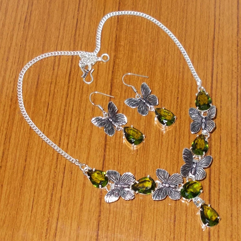 May include: A silver necklace and earrings set with green gemstone accents and butterfly designs.