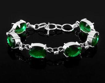 May include: Silver bracelet featuring oval-cut, emerald-green gemstones. The bracelet has a chain-link design with the gemstones set in individual silver bezels. The clasp is a simple hook and eye closure. The bracelet is displayed against a black background.
