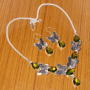 May include: A silver necklace and earrings set with green gemstone accents and butterfly designs.