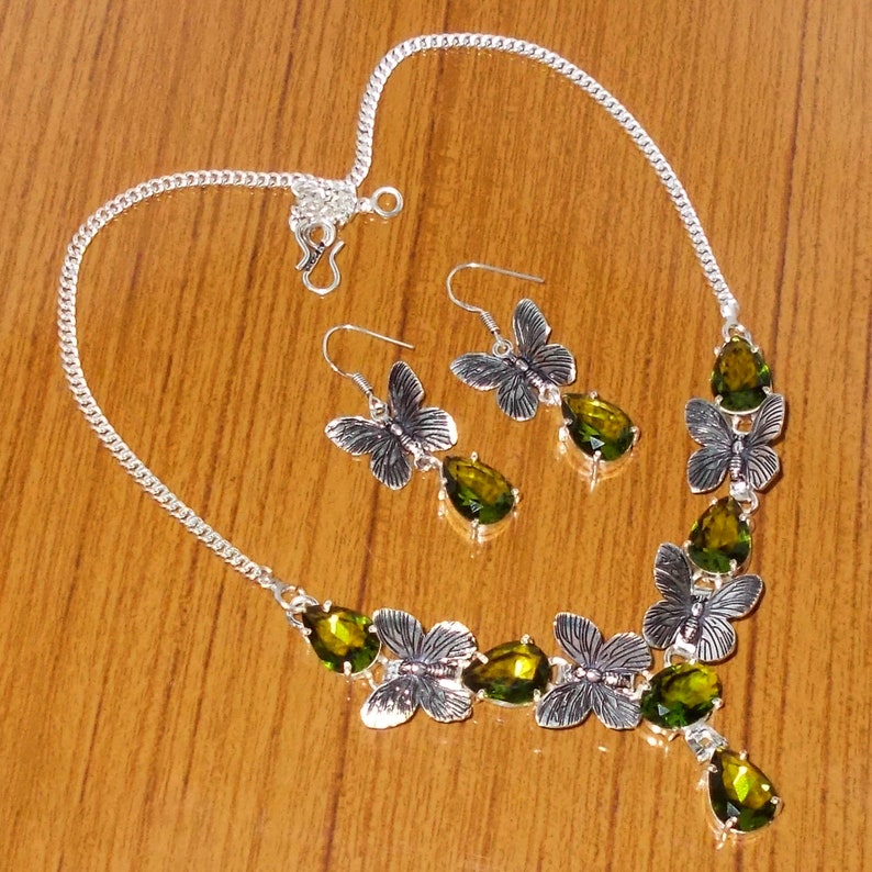 May include: A silver necklace and earrings set with green gemstone accents and butterfly designs.
