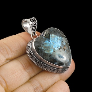May include: A silver heart-shaped pendant featuring a large, iridescent labradorite gemstone. The pendant has an intricate, ornate silver border.