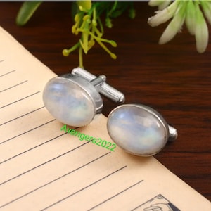 May include: A pair of silver cufflinks with oval-shaped moonstone inlays. The cufflinks have a polished silver finish.