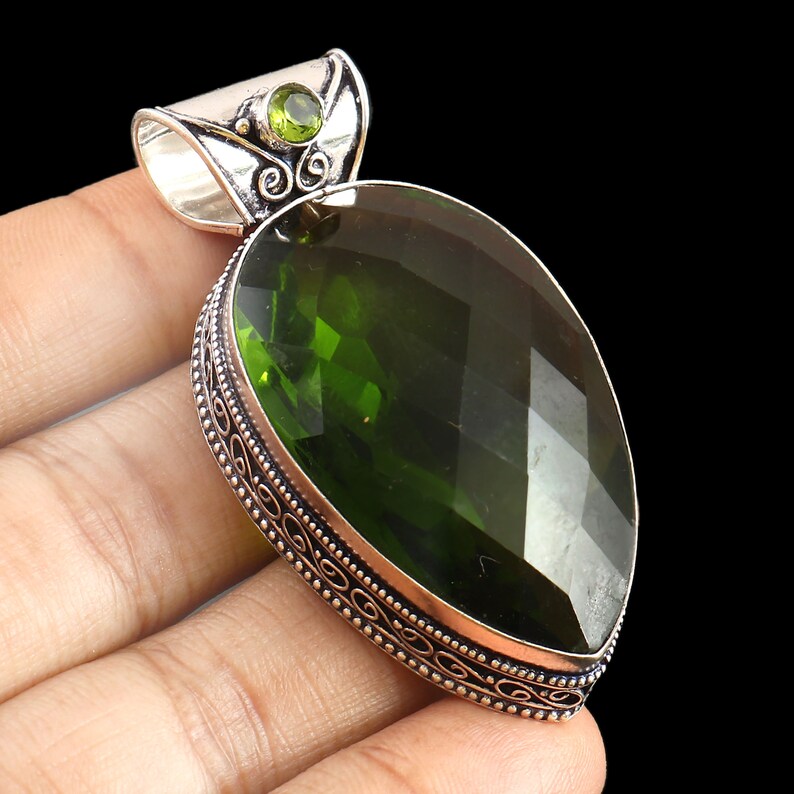 May include: A silver pendant with a large, faceted, green gemstone and a smaller green gemstone accent. The pendant has an ornate, silver border.