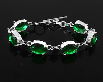 May include: Silver-toned bracelet featuring oval-cut, vibrant green gemstones. The gemstones are set in individual silver bezels and linked together with a delicate chain. The bracelet has a secure clasp closure, and the design is simple and elegant.