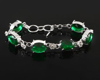 May include: A silver bracelet featuring oval-cut, emerald-green gemstones. The bracelet has a delicate chain design with a toggle clasp. The gemstones are set in a silver metal setting, creating a classic and elegant look.