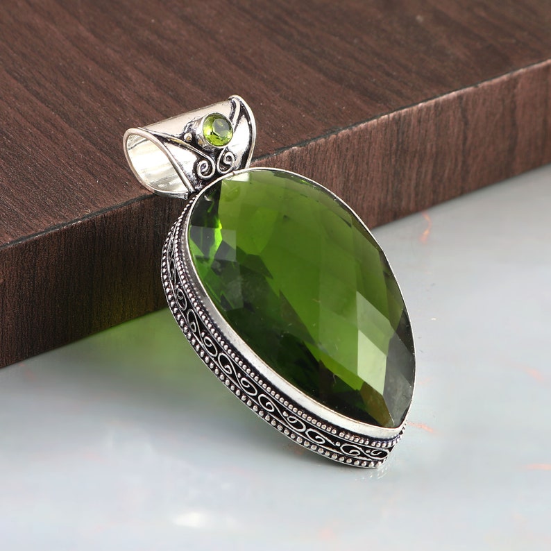 May include: A silver pendant with a large, faceted, green gemstone. The pendant has an intricate, filigree design around the gemstone.