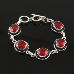 Op de afbeelding: Een zilveren armband met vijf rode ovale edelstenen. De armband heeft een schuifgesp.