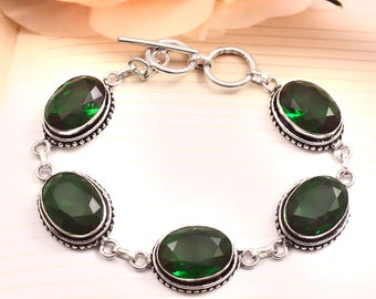 May include: A silver bracelet featuring oval-cut, emerald-green gemstones. The gemstones are set in a silver bezel with a beaded border. The bracelet has a toggle clasp closure. The design is elegant and suitable for special occasions.