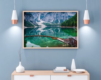 May include: A framed photograph of a mountain lake with a small wooden cabin on the shore. The lake is surrounded by snow-capped mountains and lush green trees. The water is a vibrant blue-green color and reflects the surrounding scenery.